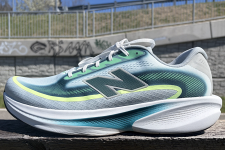 New Balance Ellipse review: running shoe in blue-teal gradient with neon-yellow accent, placed on a wooden railing outdoors.